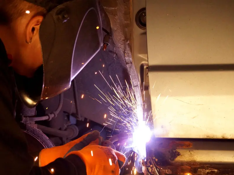Welder in a helmet working on a heavy steel section, with bright sparks