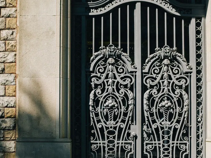 Ornate black steel double gate with scrolled panels in a stone doorway