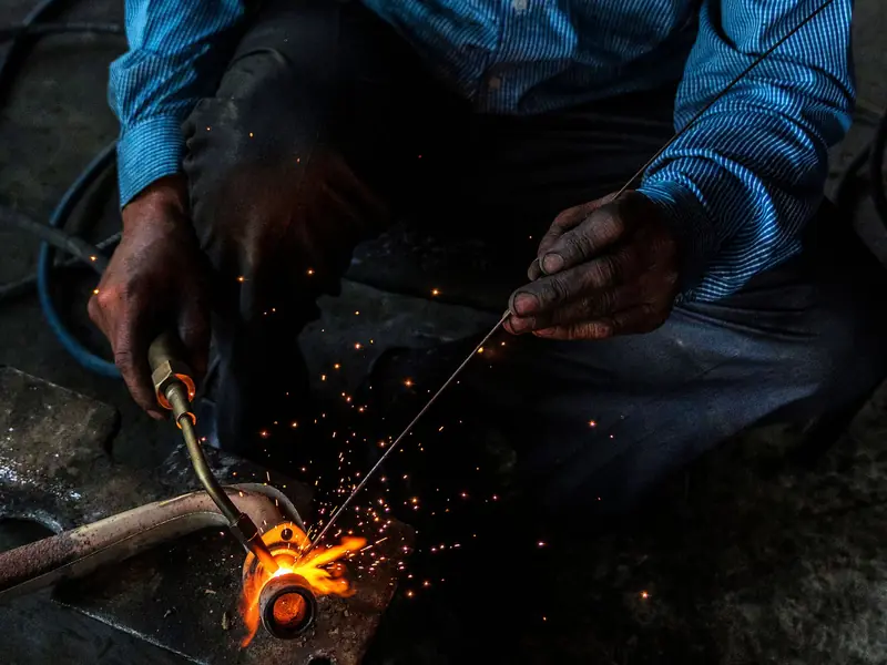 Welder using a torch and filler rod on a heavy steel part, with sparks